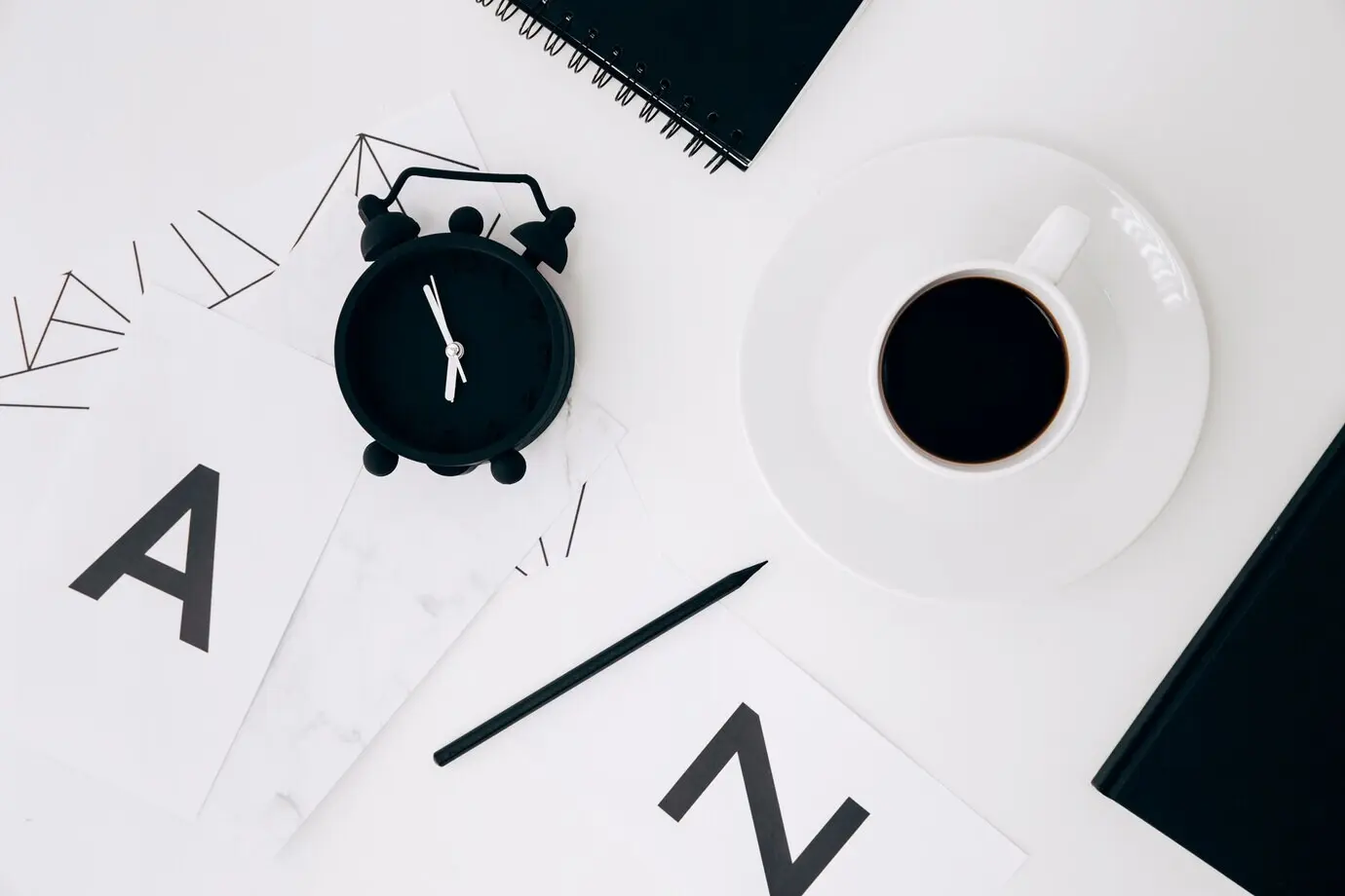 An alarm clock, a pencil, a diary, a coffee cup, and paper with the letters “a” and “n” on a white background.