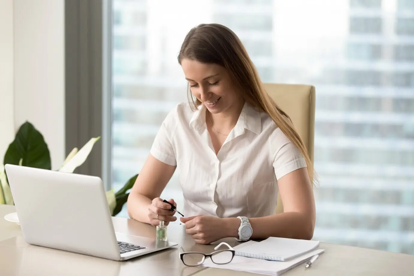 A smiling businesswoman painting her nails in the office.