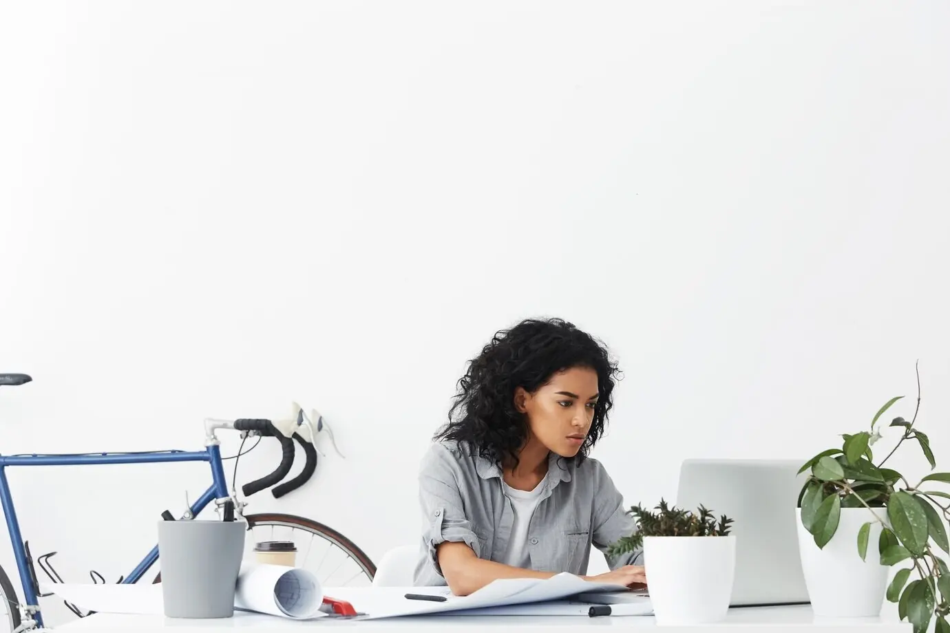 A serious young dark-skinned female designer seated in front of an open laptop computer.